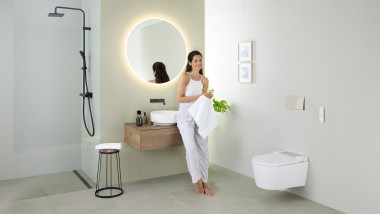 Femeie care se sprijină pe un lavoar într-o baie cu vas WC cu funcţia de bideu inclusă Geberit AquaClean Sela şi lavoar şi mobilier Geberit VariForm