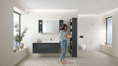 Femeia deschide un dulap înalt cu mult spațiu de depozitare în baie cu mobilier de baie Geberit Acanto